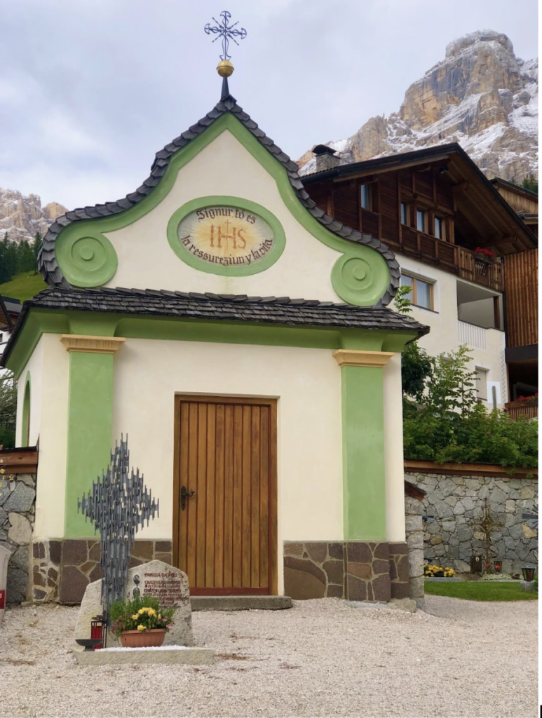 A small building with a cross on the roof at the foot at the Dolomites Mountains in a little ski town in Italy